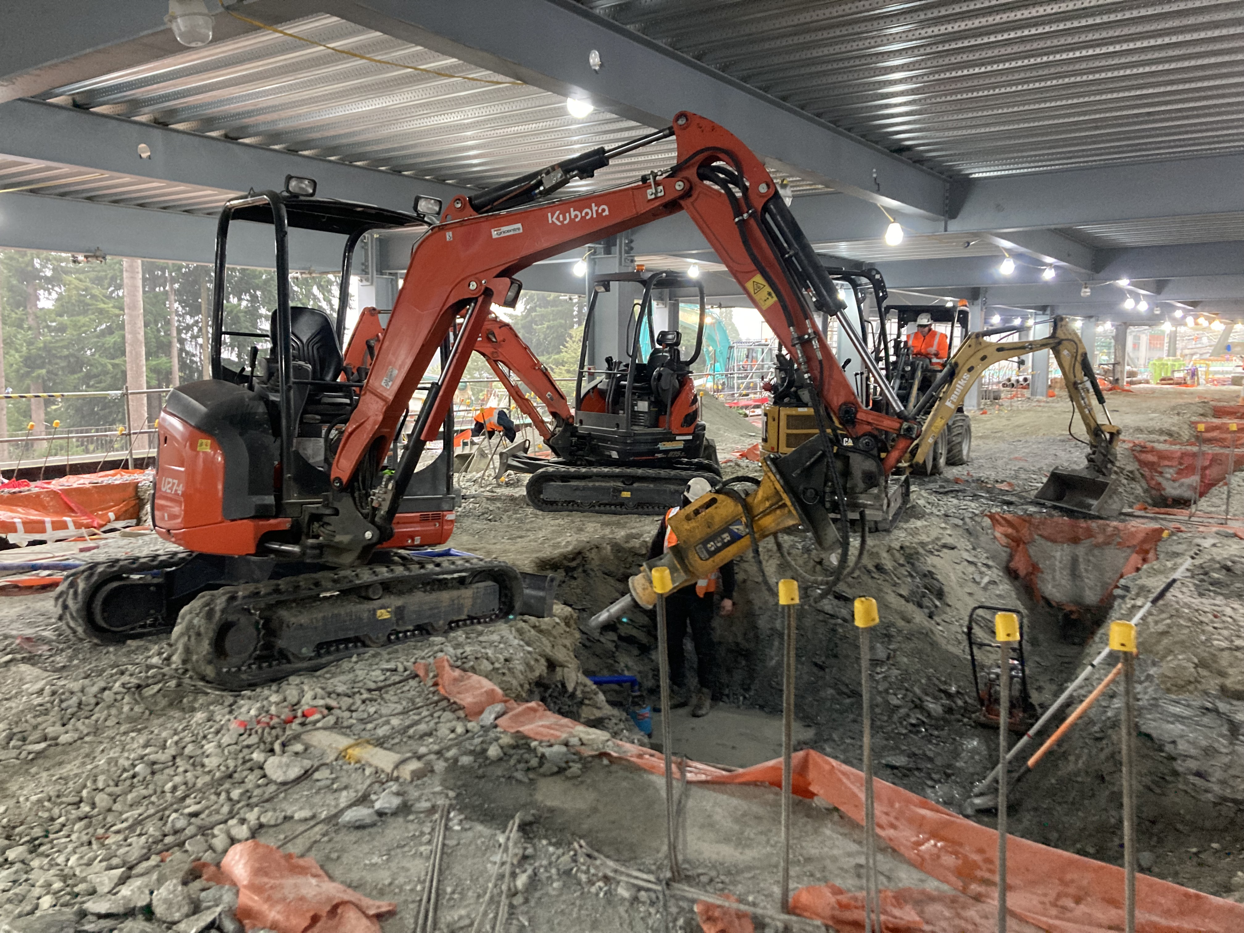 Multiple Kubota diggers working on a large commercial construction site interior, dramatic dusk lighting